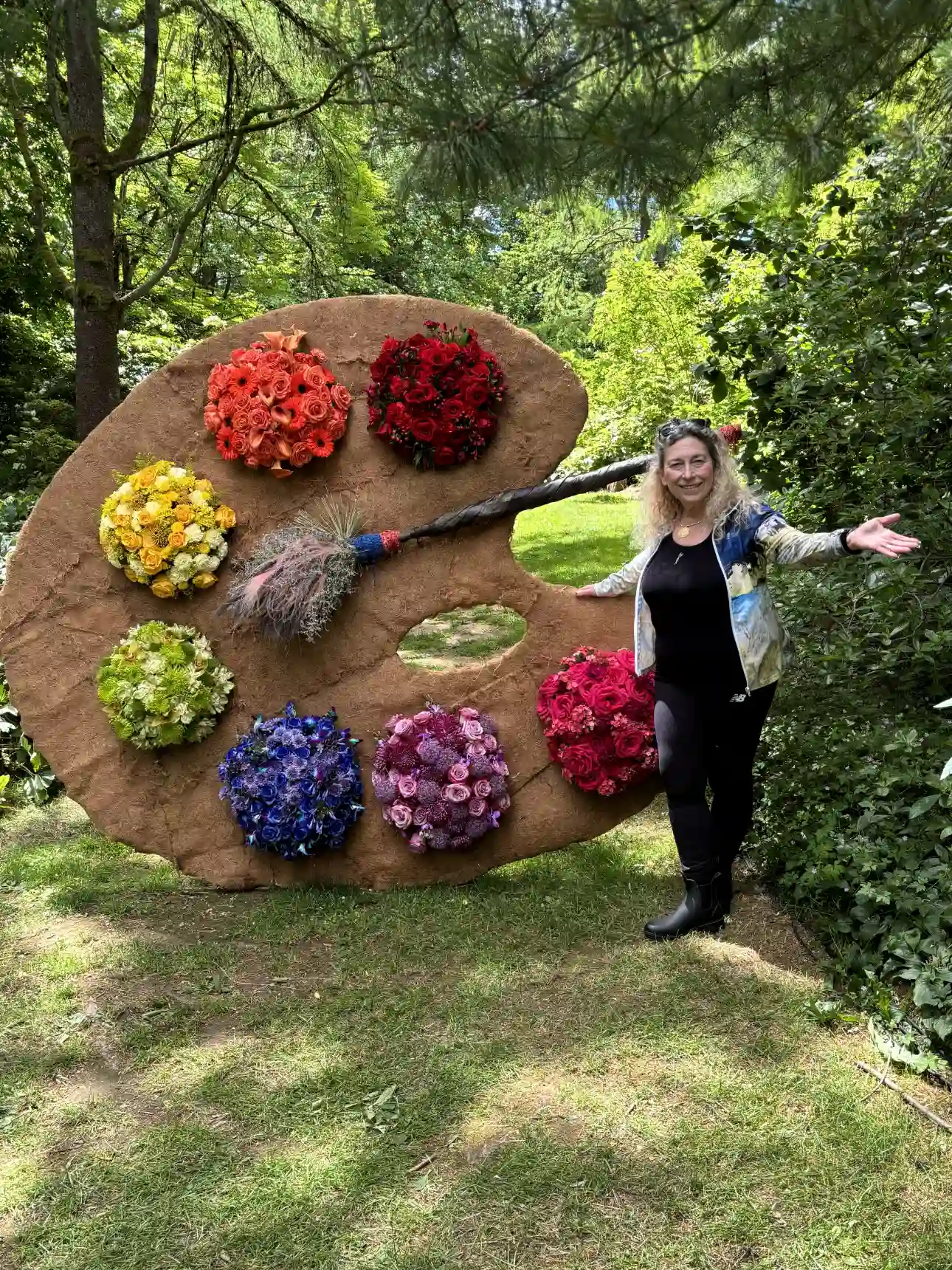 Artist Diana Zoe Coop beside an 8-foot tall artist's palette with floral bouquets in rainbow colours representing paint on a giant wooden palette. Taken at Van Dusen Gardens Vancouver BC Canada